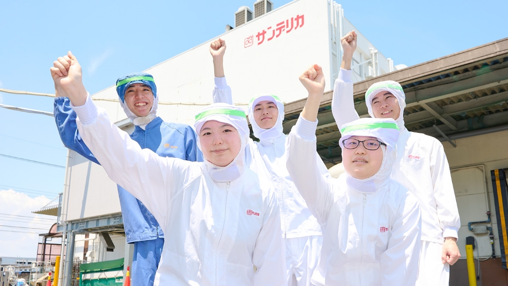 工場の前で笑顔で拳を上げる5人の社員