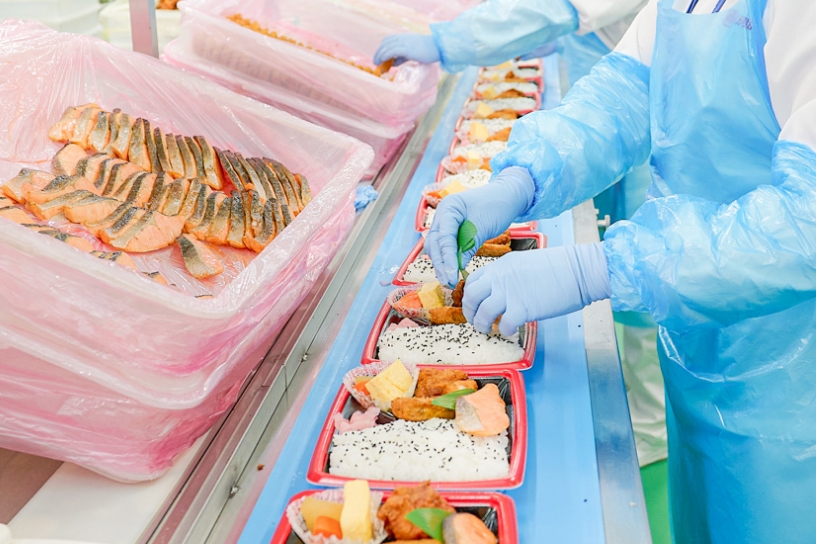 お弁当の盛り付け作業を人が行っている